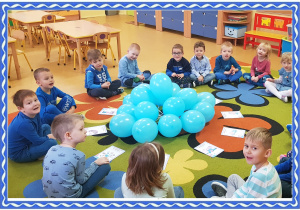 Grupa dzieci siedzi na dywanie. przed nimi niebieskie balony i obrazki przedstawiające prawa dzieckaGrupa dzieci siedzi na dywanie. przed nimi leżą niebieskie balony i obrazki przedstawiające prawa dziecka.